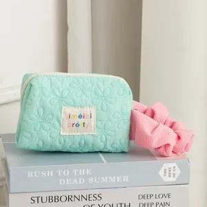 Close-up of a mint green quilted floral cosmetic bag featuring a pink scrunchie