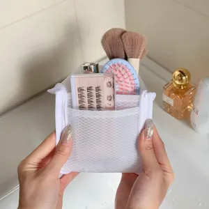 Hands holding a white mesh travel storage bag containing cosmetic accessories in a bathroom.