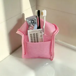 Detail of pink mesh waterproof travel toiletry bag stored with toothbrushes in bathroom.
