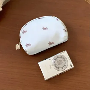 Close-up view of a light blue dog pattern cosmetic bag next to a camera for size comparison