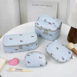 Collection of light blue dog print makeup bags in various sizes on a white table.