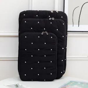Close-up of three black quilted laptop sleeves with white embroidered polka dots in various sizes