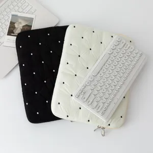 Flat lay of cream and black quilted polka dot laptop sleeves with white keyboard detail