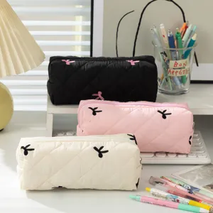 Close-up detail of three quilted large capacity pencil cases with bow embroidery on a desk
