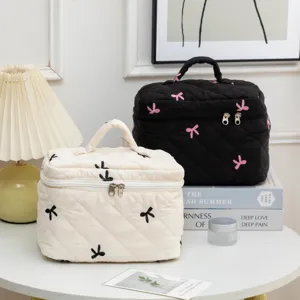 Detailed view of quilted cosmetic bags with embroidered bows in cream and black color.