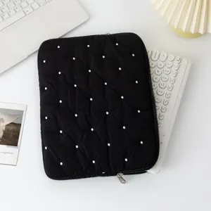 Close-up of black quilted laptop sleeve with white embroidered dots on a desk workspace.