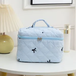 Light blue quilted cosmetic bag with black bow embroidery on white vanity table with lamp