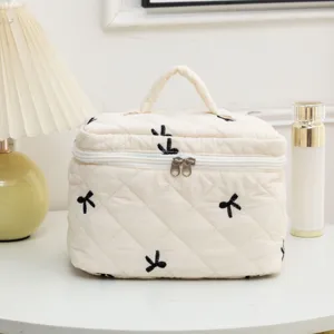 Cream quilted cosmetic bag with black embroidered bows displayed in a lifestyle setting