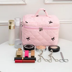 Detail of pink quilted cosmetic bag with black bow embroidery and various makeup