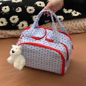Detailansicht einer blauen Reisetasche mit Herzmuster und weißem Plüsch-Anhänger