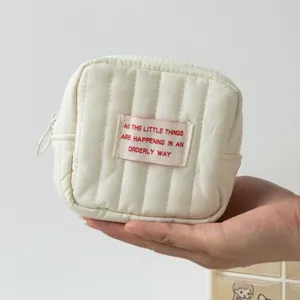 Detailansicht einer cremefarbenen gesteppten quadratischen Tasche für Münzen und Lippenstift