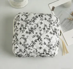 Draufsicht auf eine gesteppte weiße Kosmetiktasche aus Baumwolle mit schwarzem Blumenmuster