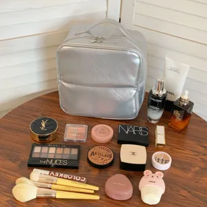Large capacity silver PU makeup organizer bag surrounded by cosmetics on a wooden table