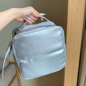 Detailed view of a silver metallic PU leather travel makeup bag organizer held by hand
