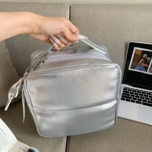 Detail shot of a silver PU makeup organizer bag held by hand in a lifestyle setting