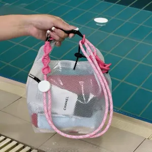 Close-up of white mesh swimming bag with pink rope handles held by hand at pool side