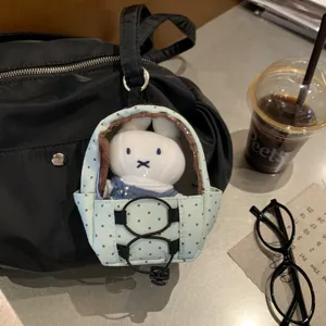 Close-up of a polka dot mini doll carrier keychain with a plush bunny inside on a bag.