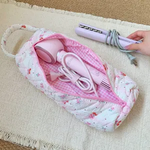 Large quilted floral storage bag holding a pink hairdryer on a cream fringed rug.