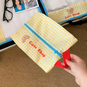 Detail of yellow gingham mesh travel organizer bag with cute bear print and red handle.