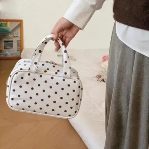 Frau hält eine große weiße Kosmetiktasche mit Punkten in einer gemütlichen Innenraum-Atmosphäre