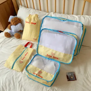 Close-up view of a yellow checkered mesh travel packing cube set on a cozy white bed