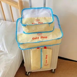 Yellow checkered travel storage bag set with blue mesh top shown on a white suitcase
