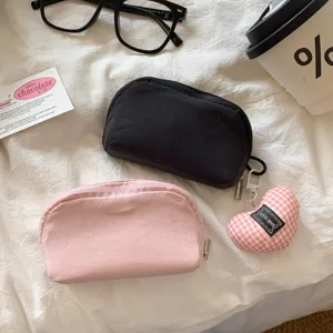 Close-up of pink and black mini cosmetic bags on a white textured fabric background.