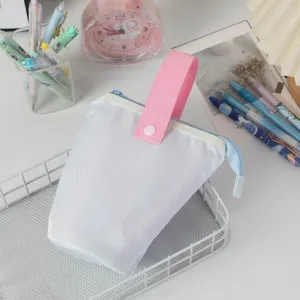Astuccio verticale bianco portatile con manico rosa e cerniera blu su scrivania bianca