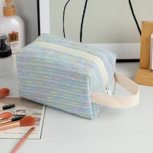 Side view of light blue tweed cosmetic bag with colorful striped embroidery and handle