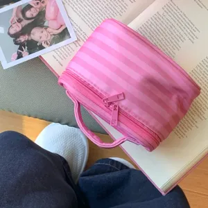 Detailansicht einer rosa gestreiften Kosmetiktasche mit Reißverschluss auf einem Buch.