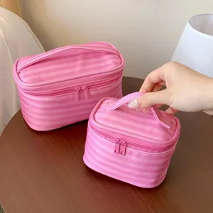 Detailansicht von zwei rosa gestreiften Kosmetiktaschen mit Griffen auf einem Holztisch