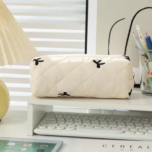 Detail view of cream quilted pencil case with black bow embroidery on a desk