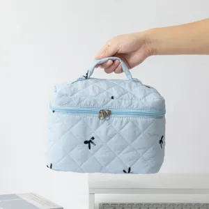 Detail view of handheld light blue quilted cosmetic bag with black bow embroidery