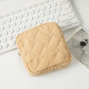 Nahaufnahme einer quadratischen gesteppten beigen Kosmetiktasche auf weißem Schreibtisch
