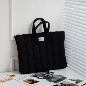 Nahaufnahme einer schwarzen, gesteppten, stoßfesten Laptoptasche mit Griffen auf dem Tisch.