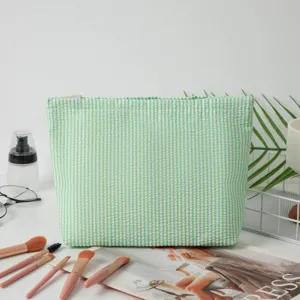 Detailansicht der grünen Seersucker-Kosmetiktasche mit Streifen in einer Lifestyle-Umgebung.