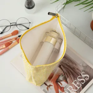 Detailaufnahme der gelb gestreiften Seersucker-Kosmetiktasche mit großem Fassungsvermögen.