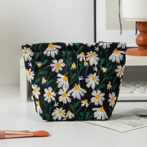 Nahaufnahme der feinen weißen Gänseblümchen-Stickerei auf schwarzer Canvas-Kosmetiktasche
