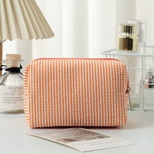 Nahaufnahme der orange gestreiften Seersucker-Kosmetiktasche auf einem hellen Waschtisch