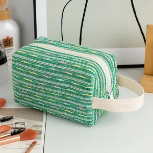 Detail view of green tweed makeup bag with colorful striped embroidery and white handle