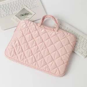 Stylish pink quilted laptop sleeve with handles placed on a white desk beside a keyboard