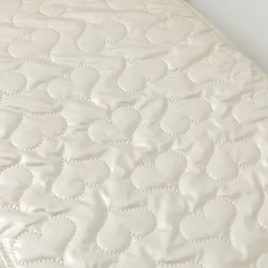 Detailed macro view of cream heart-shaped quilted fabric with soft pearly satin finish