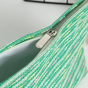 Dettaglio della cerniera argentata e della trama tessuta verde della borsa da trucco