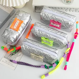 Detail showing four silver quilted pencil bags with colorful rope handles on a desk