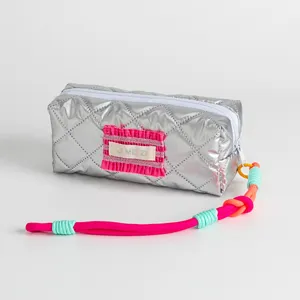 Detail of a silver quilted stationery pouch with a vibrant pink and orange braided handle