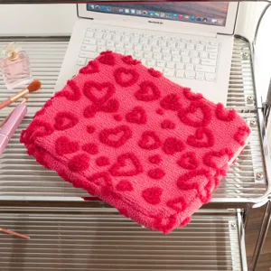 Macro view of pink plush laptop sleeve with heart patterns on a white desk setup