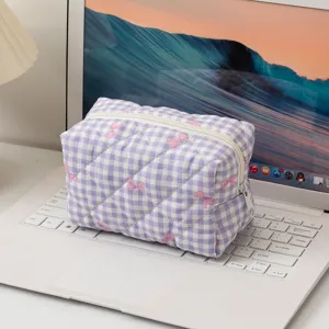 Dettaglio di una trousse per cosmetici a quadretti viola con fiocchi rosa su un laptop