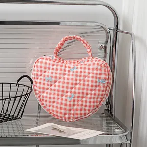 Detail der herzförmigen gesteppten Kosmetiktasche mit rotem Karo und blauen Schleifen.