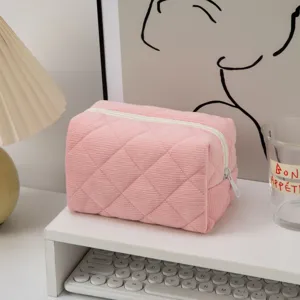 Soft pink quilted corduroy cosmetic storage bag with zipper detail on a desk