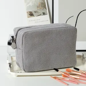 Seersucker striped cosmetic bag displayed with professional makeup brushes on a tray